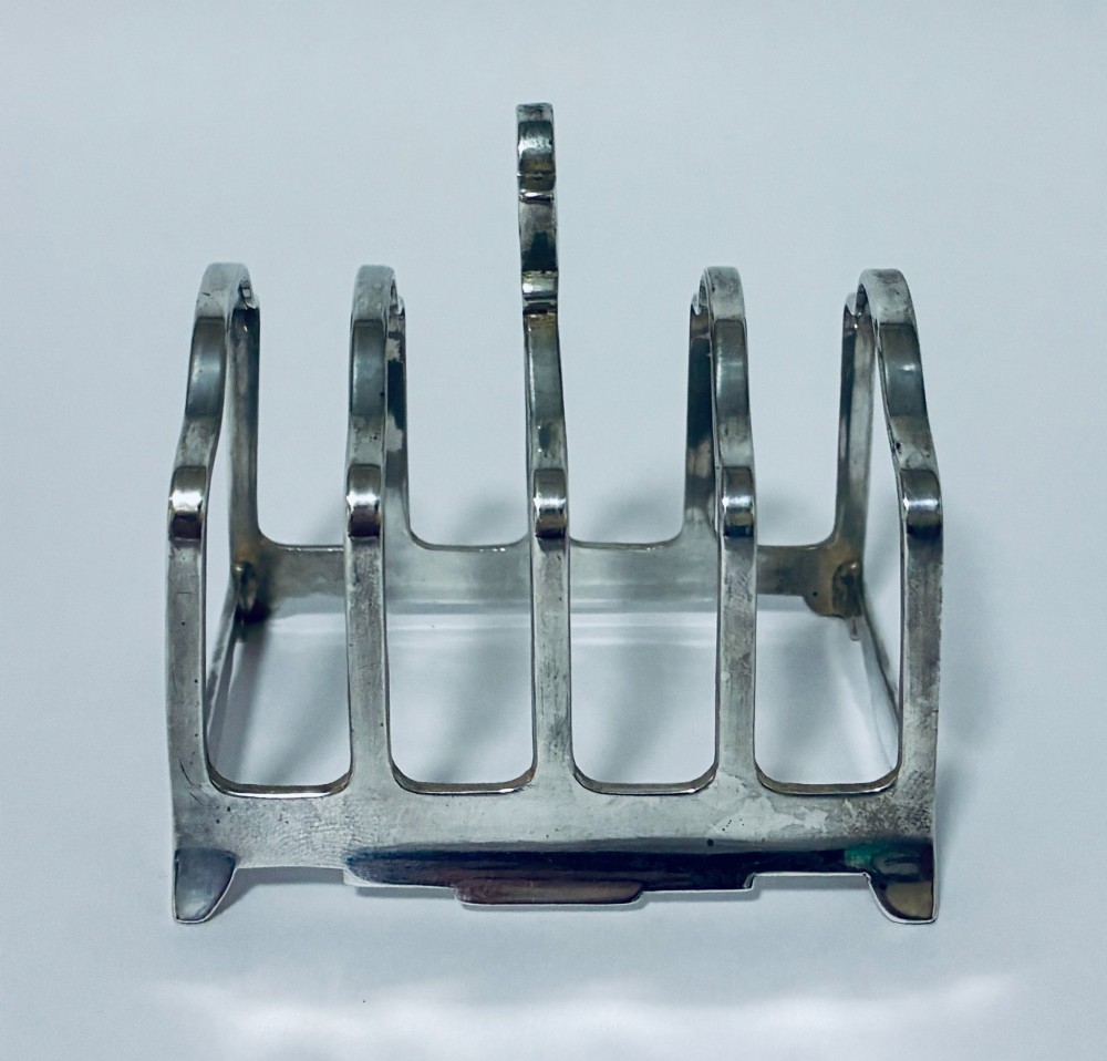 A Victorian sterling silver toast rack featuring four arched dividers, a central loop handle, and stamped hallmarks along the front base rail. View V