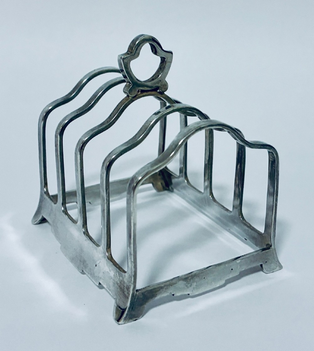 A Victorian sterling silver toast rack featuring four arched dividers, a central loop handle, and stamped hallmarks along the front base rail. View VI