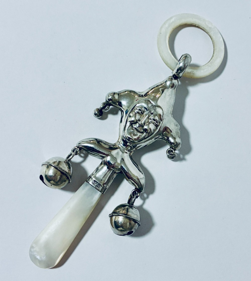 An antique sterling silver baby rattle shaped like a jester with hanging bells, a mother-of-pearl handle, and an attached ring.