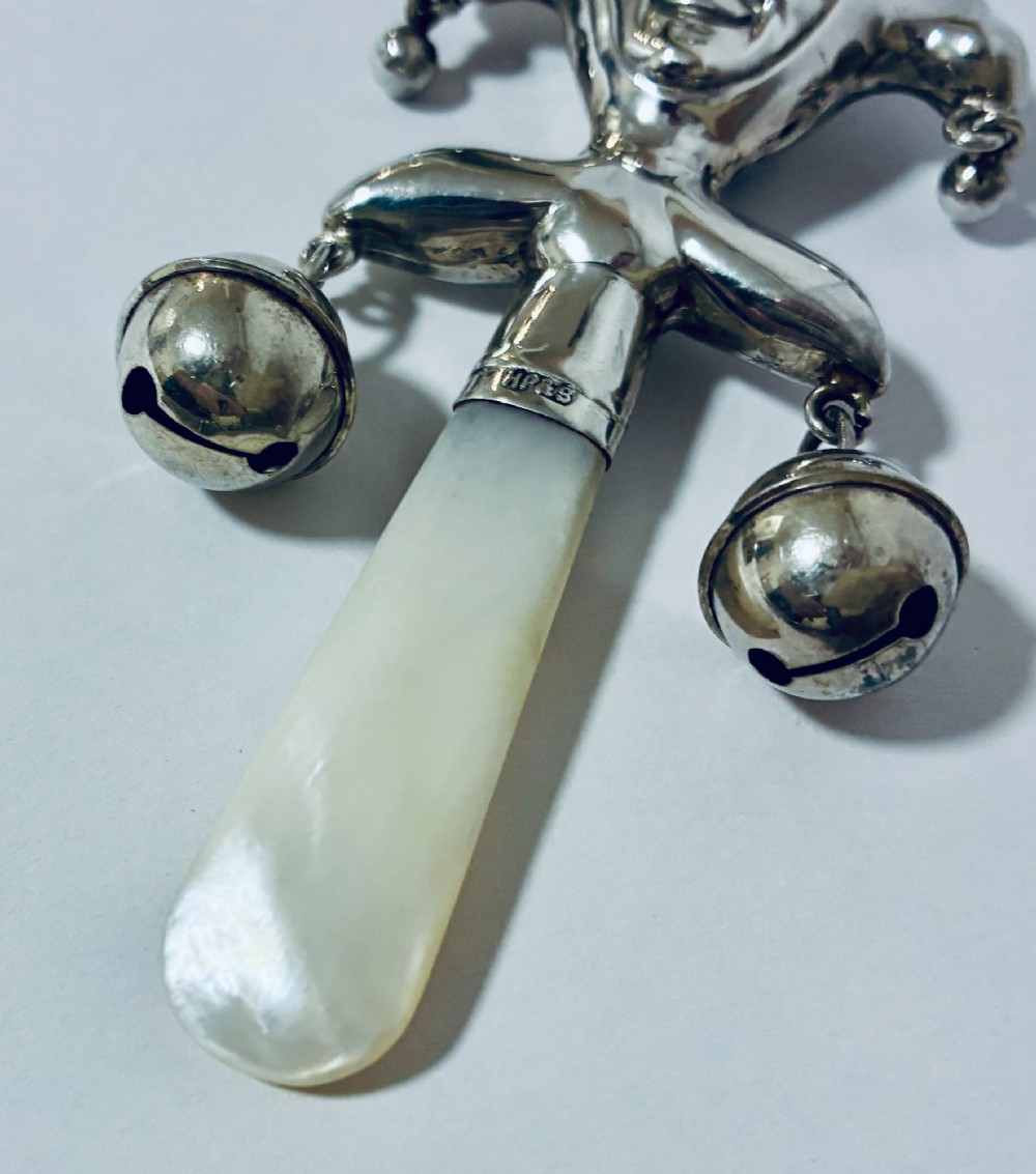 An antique sterling silver baby rattle shaped like a jester with hanging bells, a mother-of-pearl handle, and an attached ring. View III