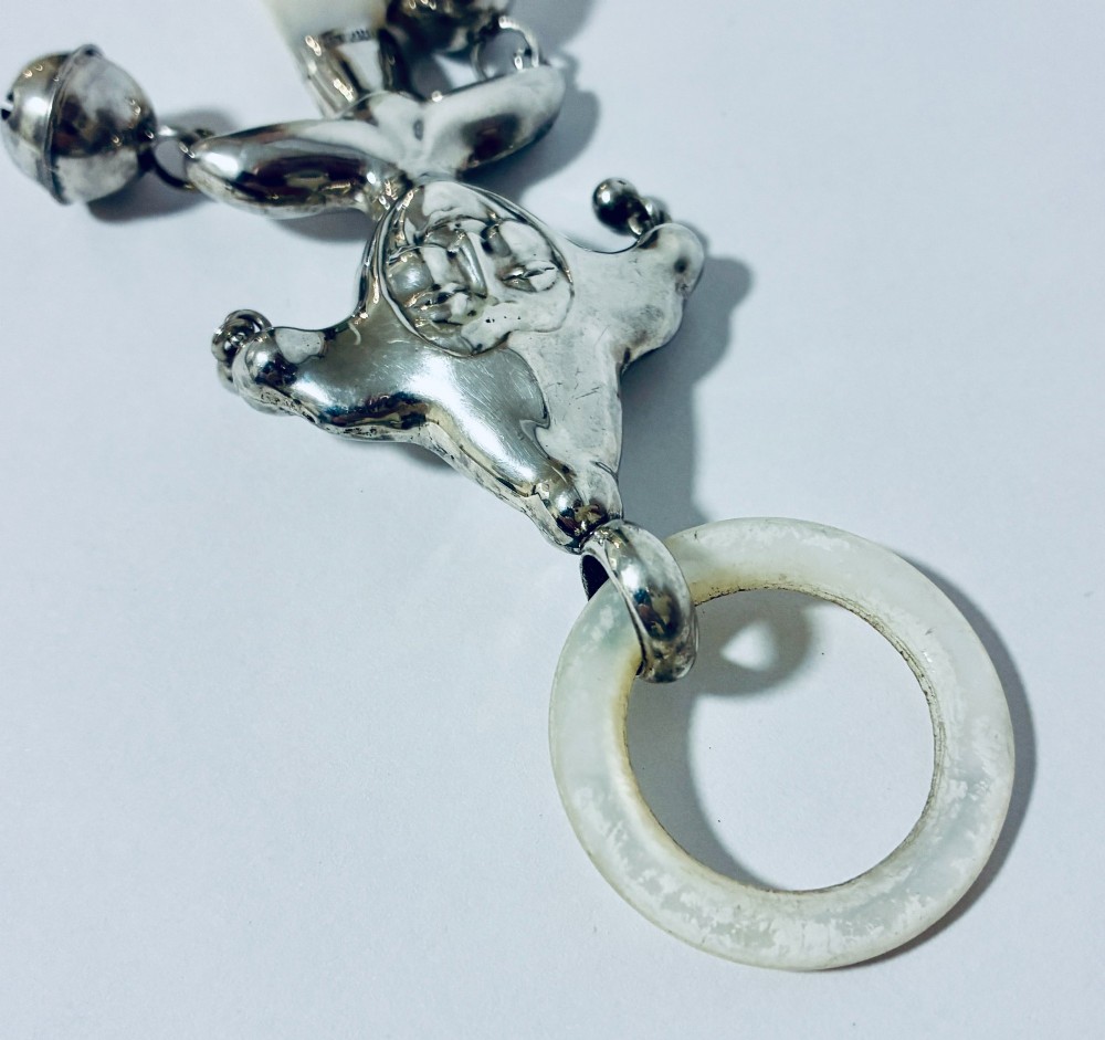 An antique sterling silver baby rattle shaped like a jester with hanging bells, a mother-of-pearl handle, and an attached ring. View IV