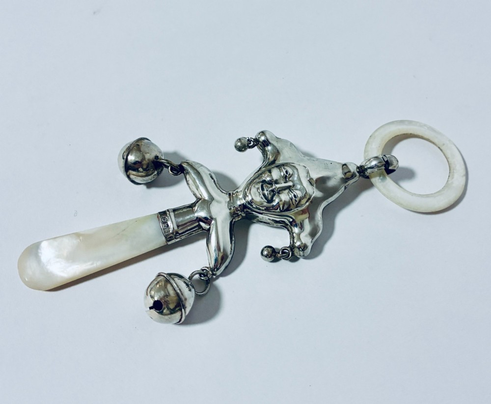 An antique sterling silver baby rattle shaped like a jester with hanging bells, a mother-of-pearl handle, and an attached ring. View V
