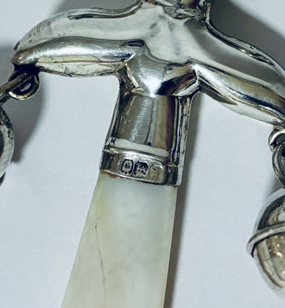 An antique sterling silver baby rattle shaped like a jester with hanging bells, a mother-of-pearl handle, and an attached ring. View VI