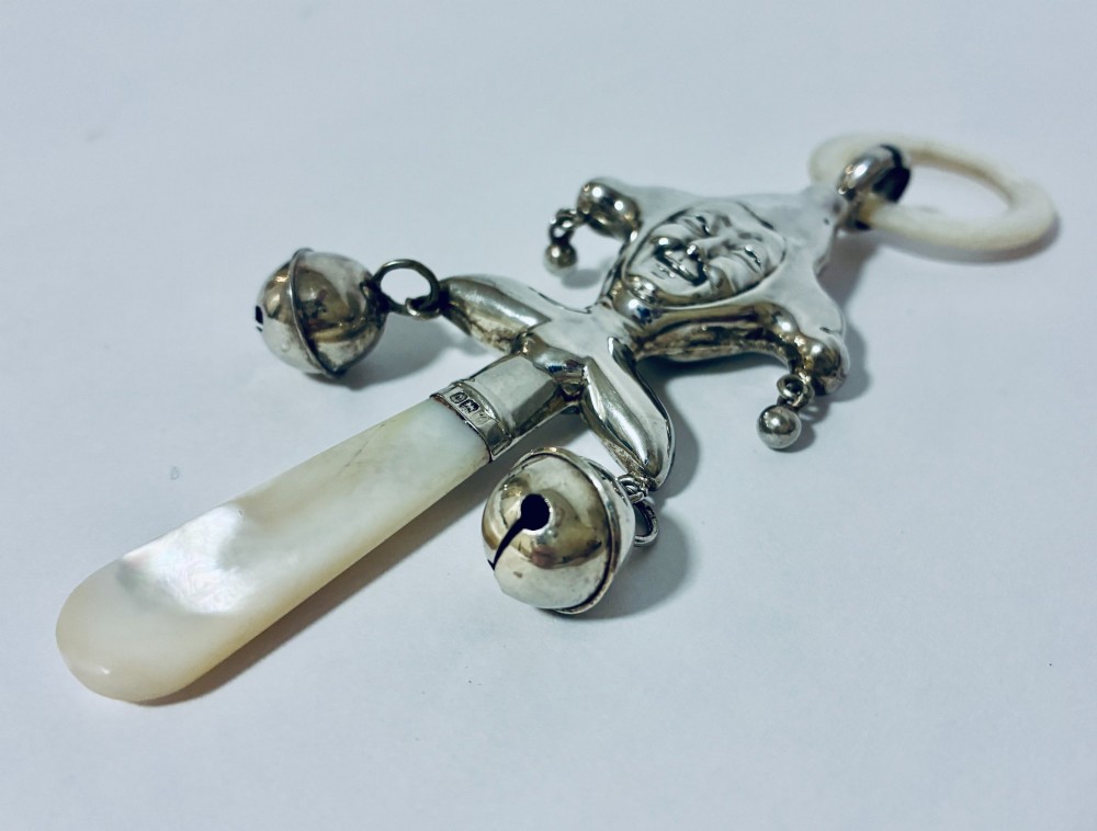 An antique sterling silver baby rattle shaped like a jester with hanging bells, a mother-of-pearl handle, and an attached ring. View VII