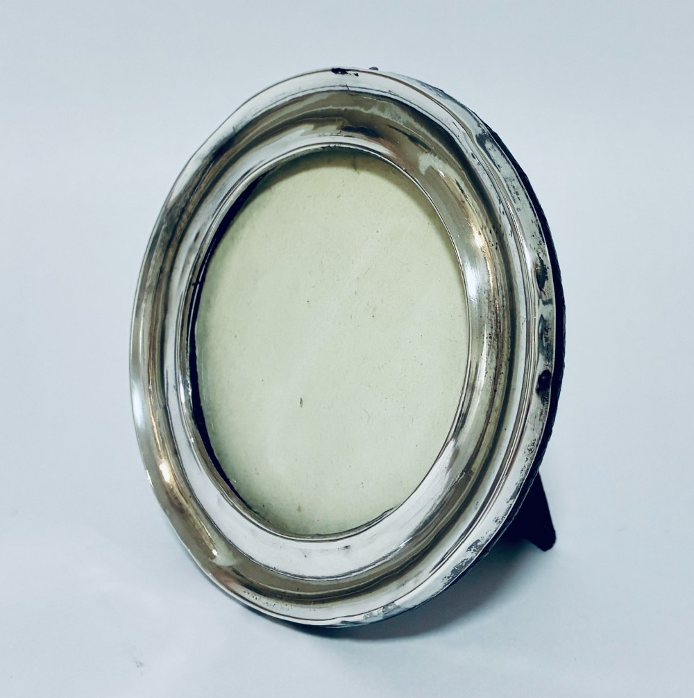 A circular antique silver photo frame with a raised convex moulding rim and a black easel backing.