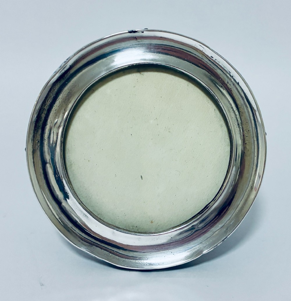 A circular antique silver photo frame with a raised convex moulding rim and a black easel backing. View II