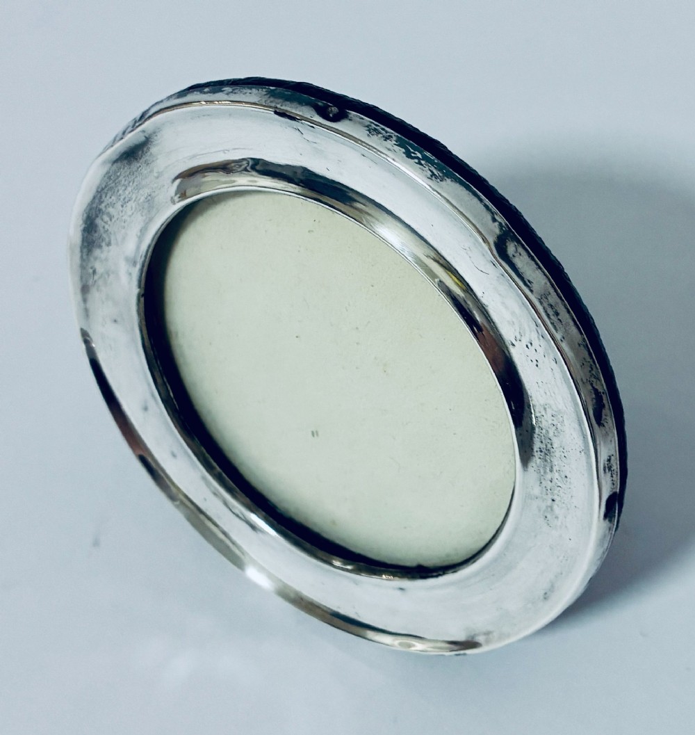 A circular antique silver photo frame with a raised convex moulding rim and a black easel backing. View III