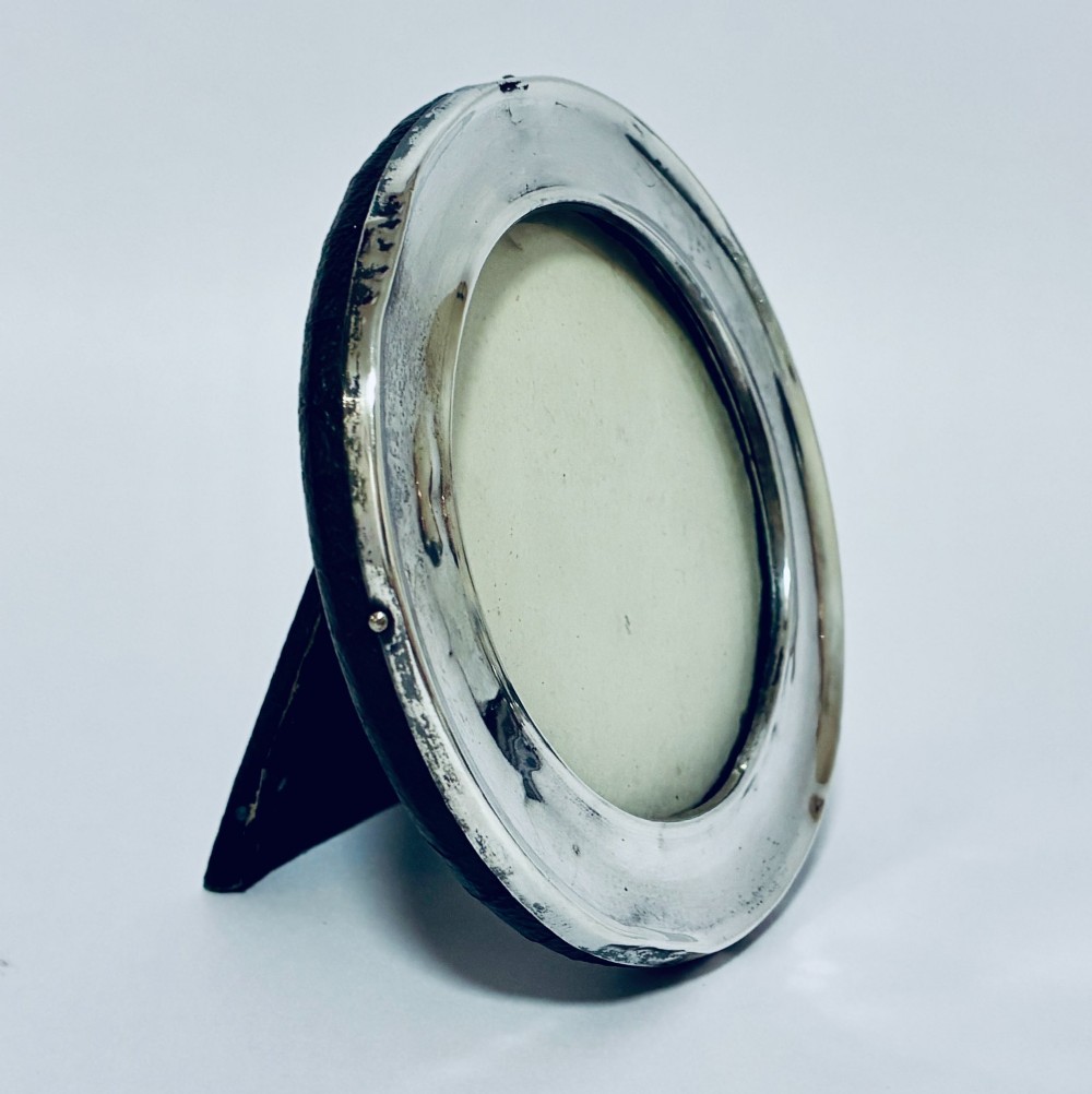 A circular antique silver photo frame with a raised convex moulding rim and a black easel backing. View IV