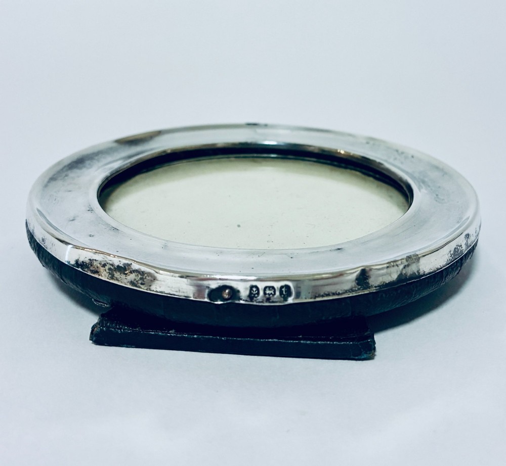 A circular antique silver photo frame with a raised convex moulding rim and a black easel backing. View IX