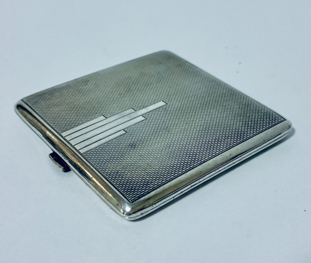 A square Art Deco silver powder compact with an engine-turned guilloche surface and a stepped geometric motif.