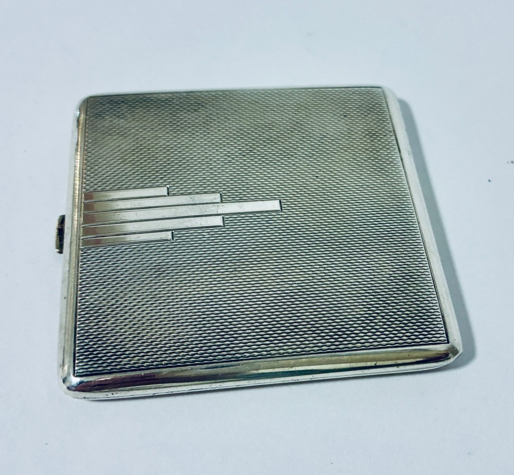 A square Art Deco silver powder compact with an engine-turned guilloche surface and a stepped geometric motif. View VI