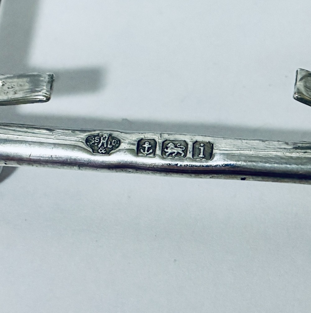 An antique silver toast rack featuring five arched divisions, a central loop handle, and a rectangular base supported by four ball feet. View VII