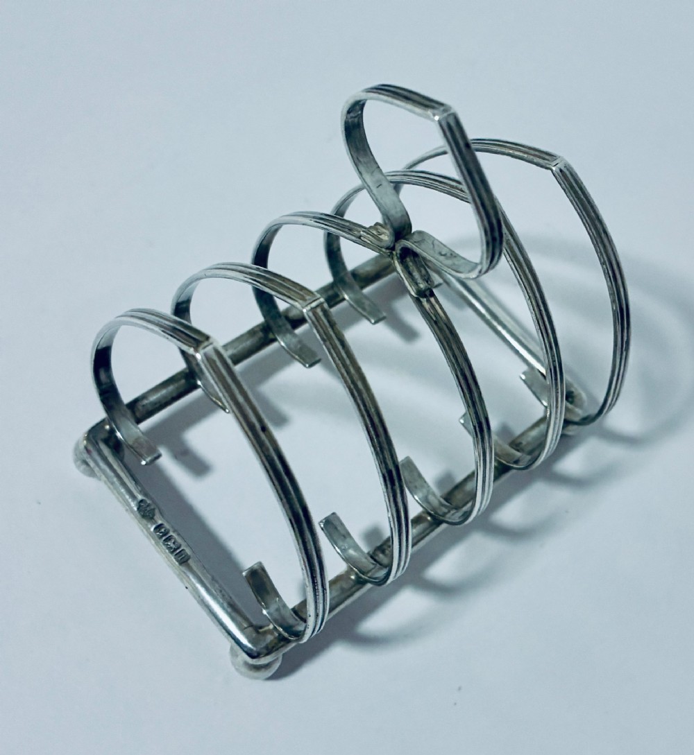 An antique silver toast rack featuring five arched divisions, a central loop handle, and a rectangular base supported by four ball feet. View VIII