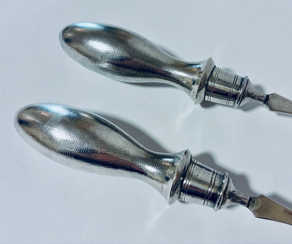 A pair of antique silver salad servers displaying planished hammered handles and polished metal serving ends. View III