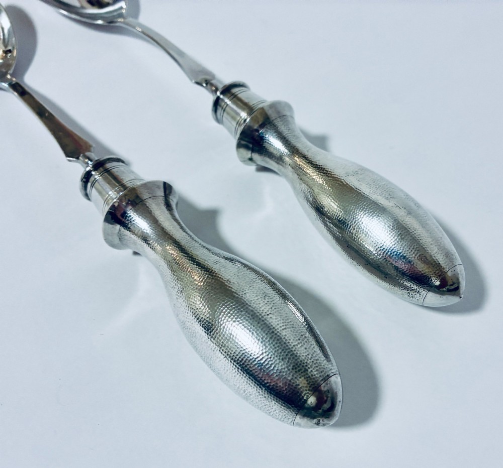 A pair of antique silver salad servers displaying planished hammered handles and polished metal serving ends. View V
