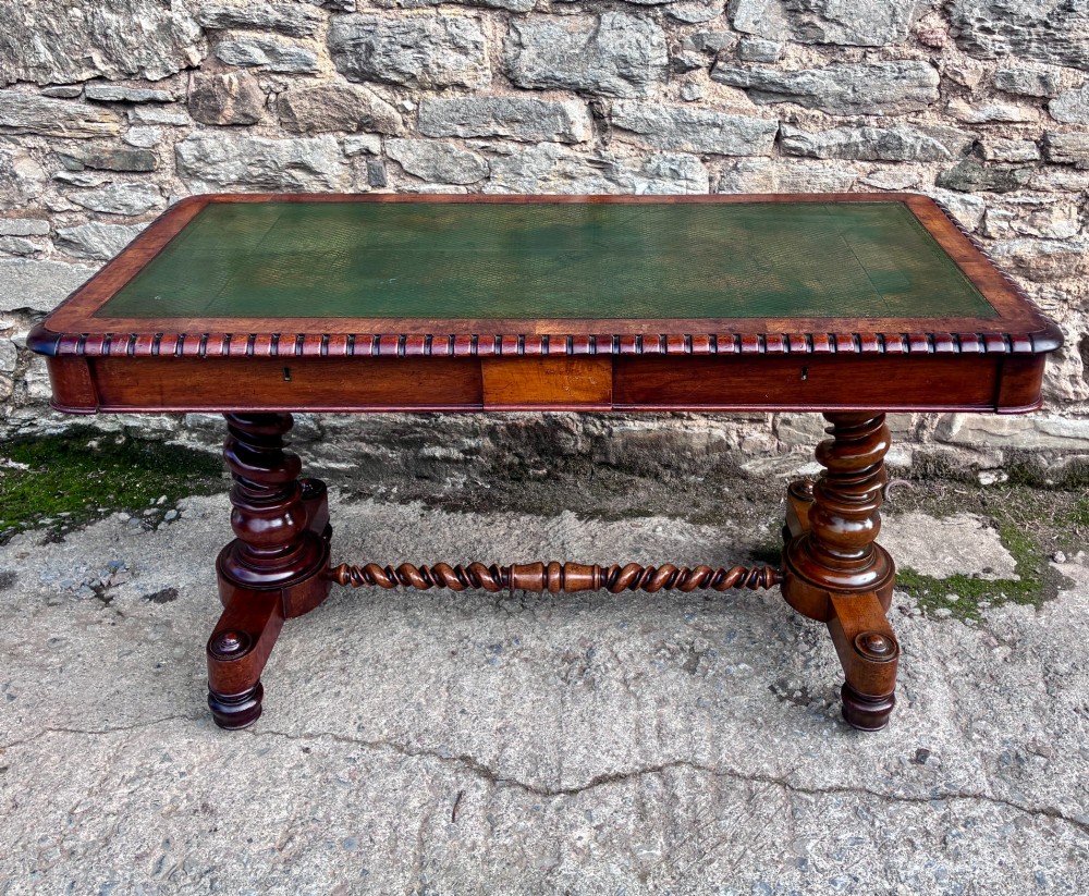 A Victorian walnut library writing table featuring a green inset leather top, carved gadrooned edge, twin drawers, and spiral barley twist legs connected by a central stretcher.
