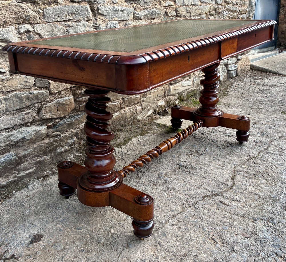 A Victorian walnut library writing table featuring a green inset leather top, carved gadrooned edge, twin drawers, and spiral barley twist legs connected by a central stretcher. View IV