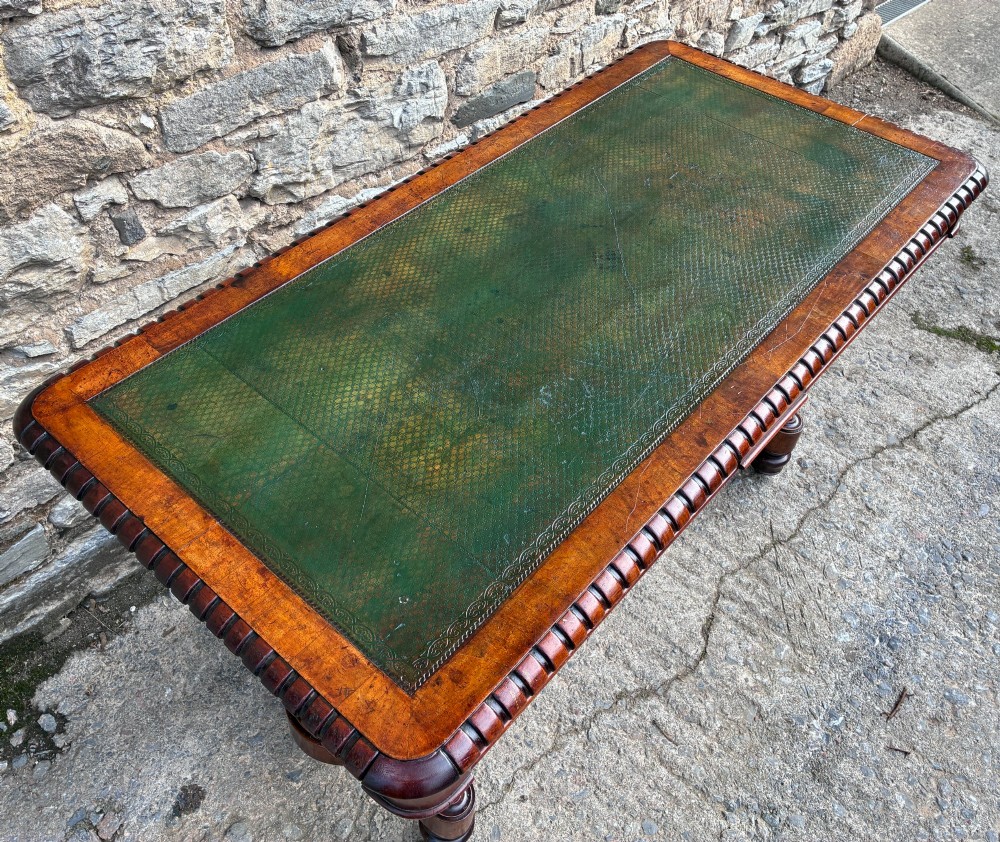 A Victorian walnut library writing table featuring a green inset leather top, carved gadrooned edge, twin drawers, and spiral barley twist legs connected by a central stretcher. View V