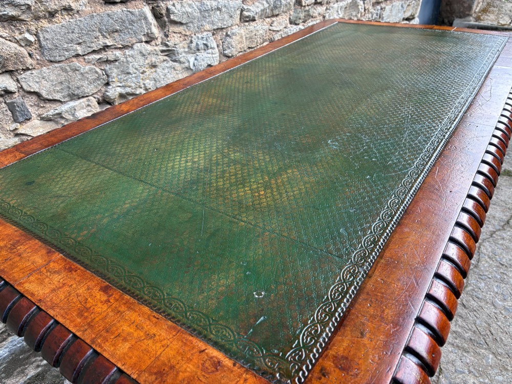 A Victorian walnut library writing table featuring a green inset leather top, carved gadrooned edge, twin drawers, and spiral barley twist legs connected by a central stretcher. View VI