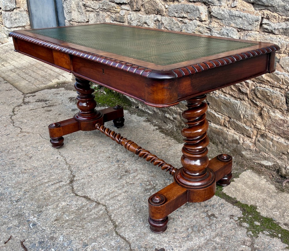 A Victorian walnut library writing table featuring a green inset leather top, carved gadrooned edge, twin drawers, and spiral barley twist legs connected by a central stretcher. View VII