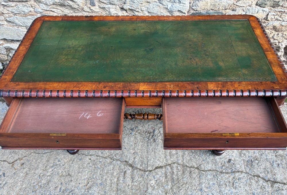 A Victorian walnut library writing table featuring a green inset leather top, carved gadrooned edge, twin drawers, and spiral barley twist legs connected by a central stretcher. View X