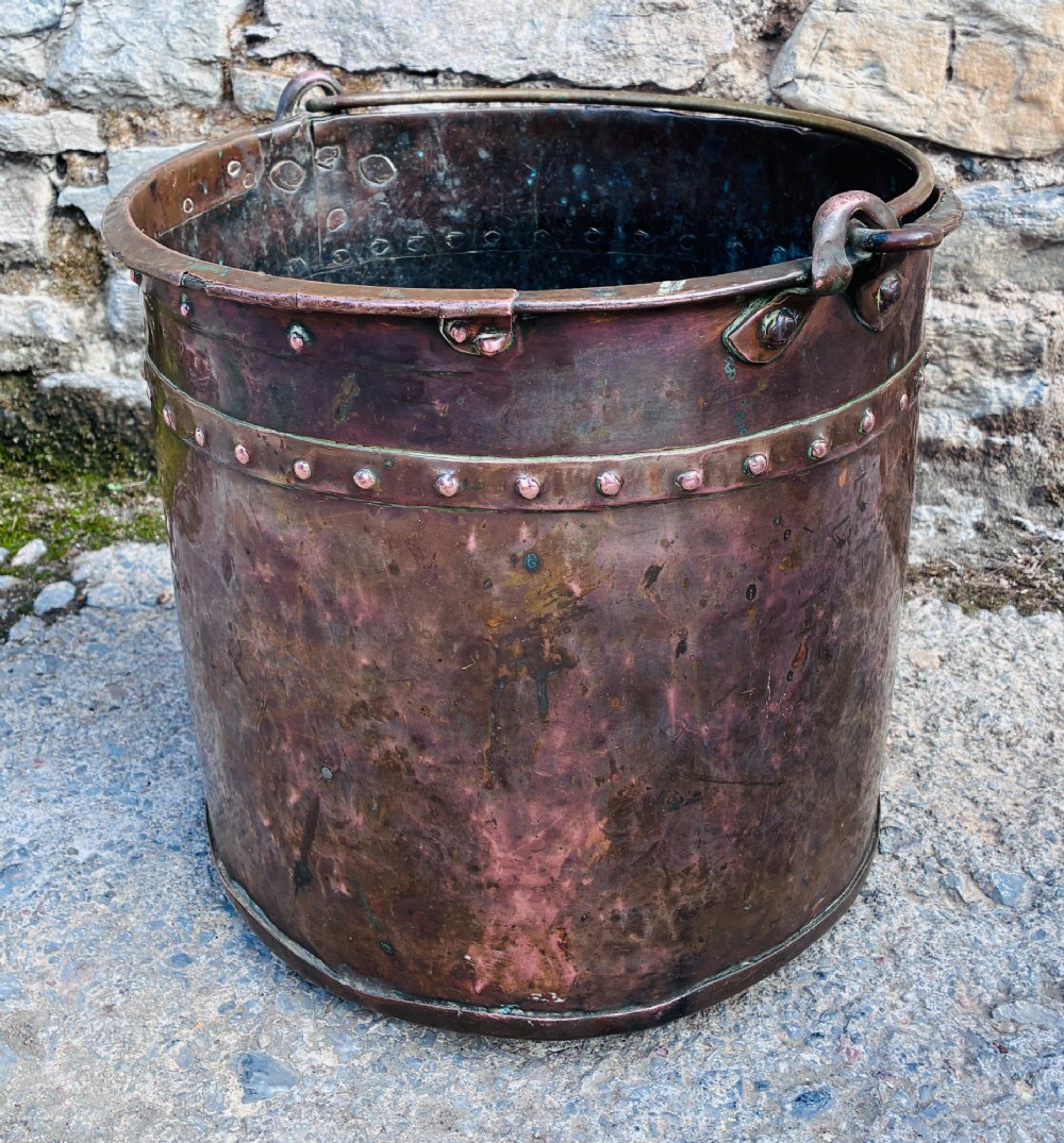 An antique cylindrical copper bucket featuring heavy copper rivets along the upper rim band and a metal swing handle. View II
