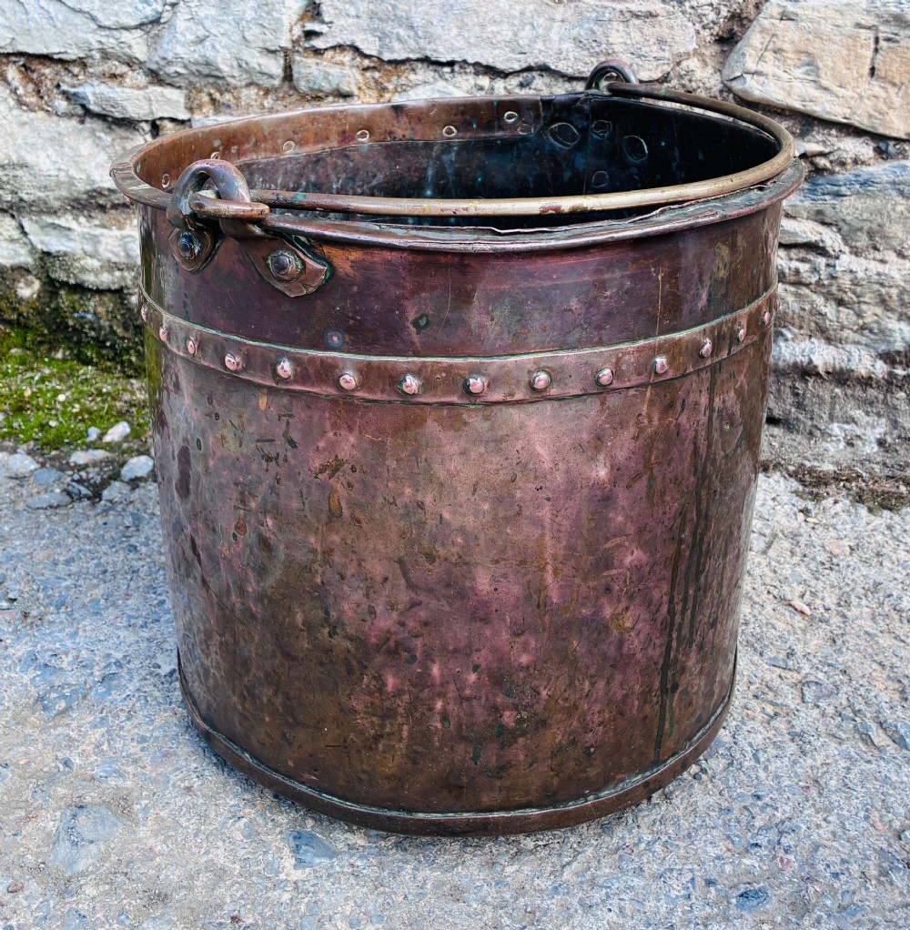 An antique cylindrical copper bucket featuring heavy copper rivets along the upper rim band and a metal swing handle. View III