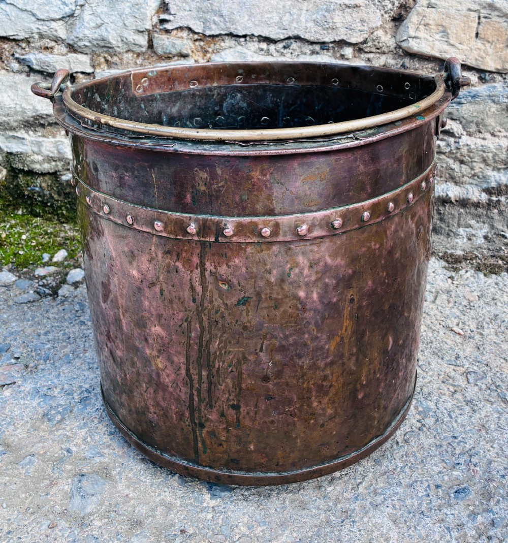 An antique cylindrical copper bucket featuring heavy copper rivets along the upper rim band and a metal swing handle. View IV