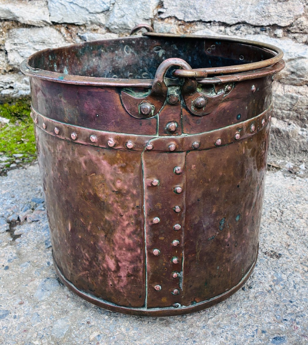 An antique cylindrical copper bucket featuring heavy copper rivets along the upper rim band and a metal swing handle. View VIII
