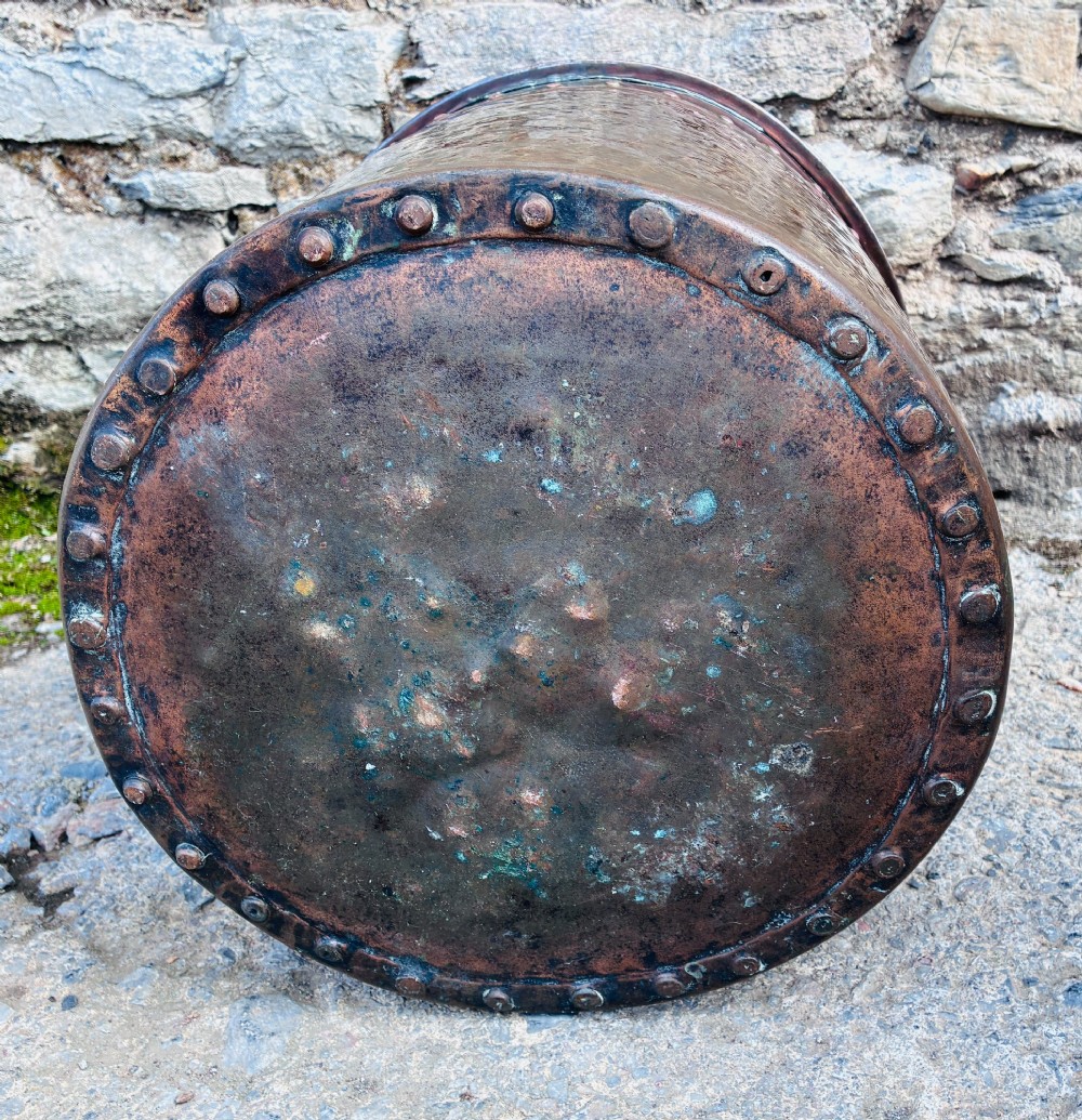 An antique cylindrical copper bucket featuring heavy copper rivets along the upper rim band and a metal swing handle. View X
