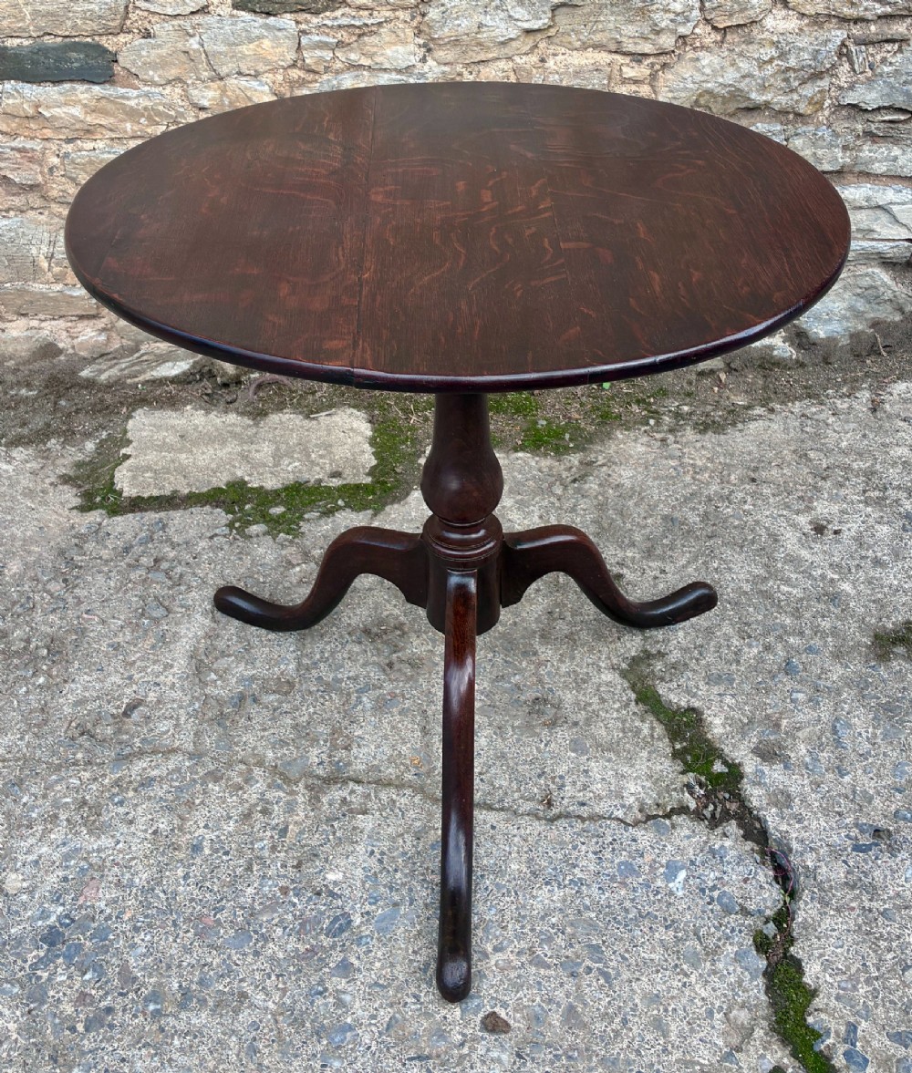 A dark brown Georgian oak tilt-top tripod table featuring a circular top, turned baluster column, and three cabriole legs.