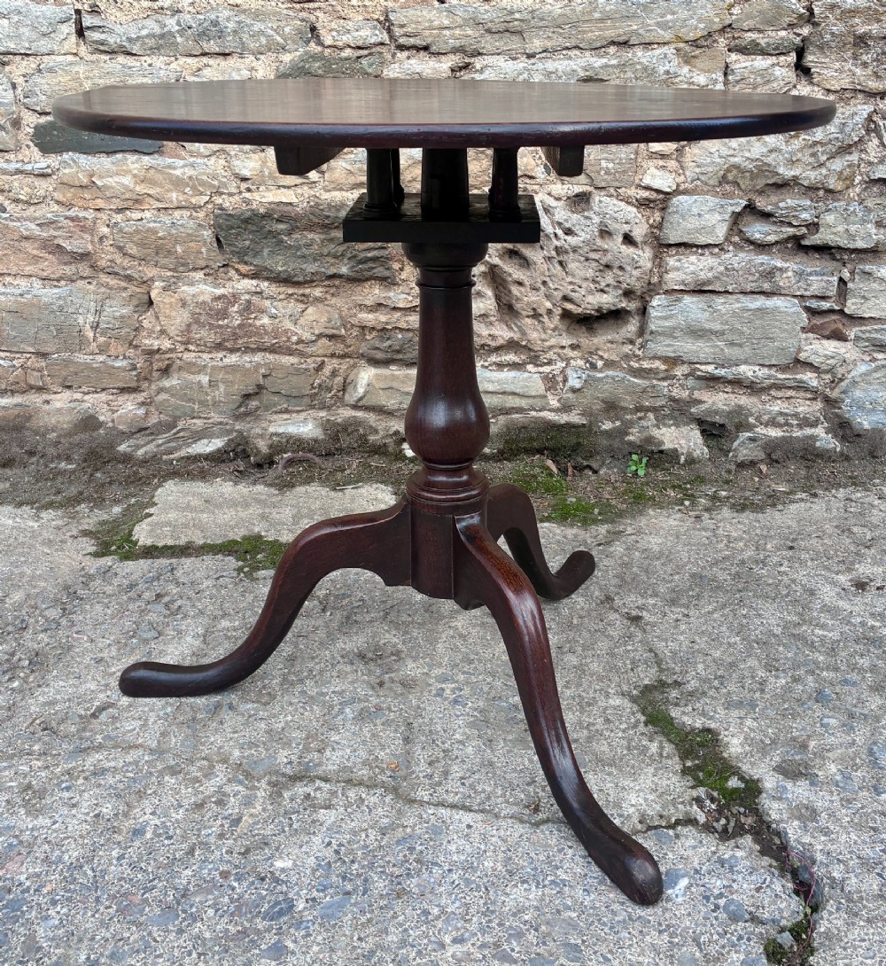 A dark brown Georgian oak tilt-top tripod table featuring a circular top, turned baluster column, and three cabriole legs. View VI