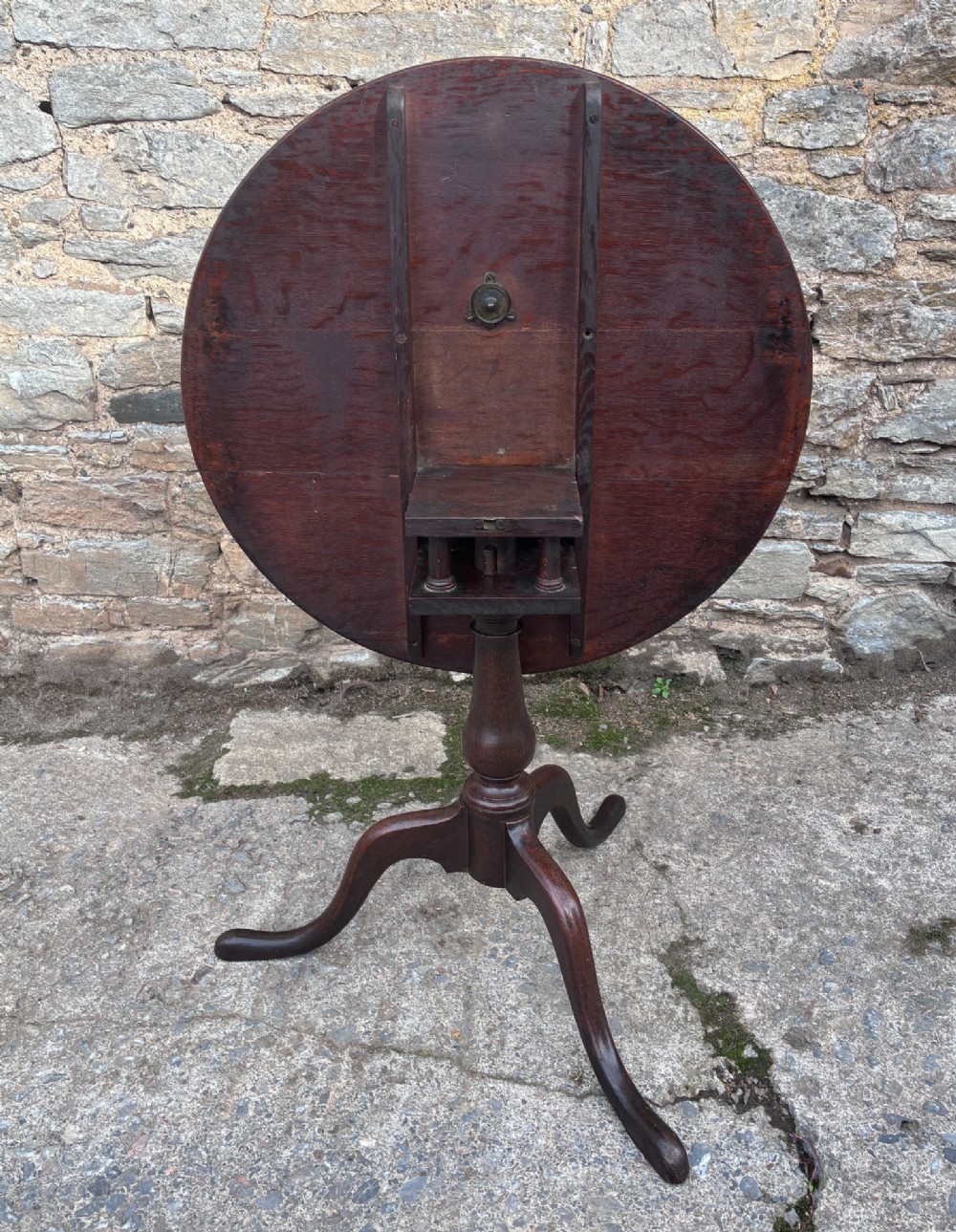 A dark brown Georgian oak tilt-top tripod table featuring a circular top, turned baluster column, and three cabriole legs. View VII