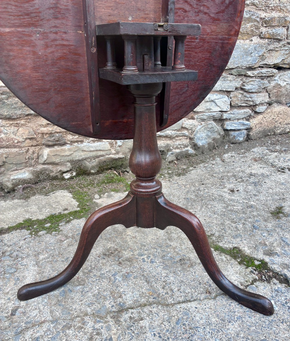 A dark brown Georgian oak tilt-top tripod table featuring a circular top, turned baluster column, and three cabriole legs. View VIII