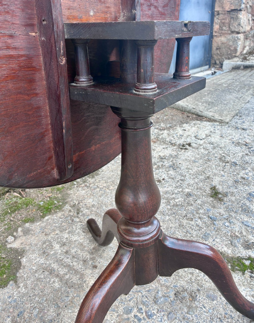 A dark brown Georgian oak tilt-top tripod table featuring a circular top, turned baluster column, and three cabriole legs. View X