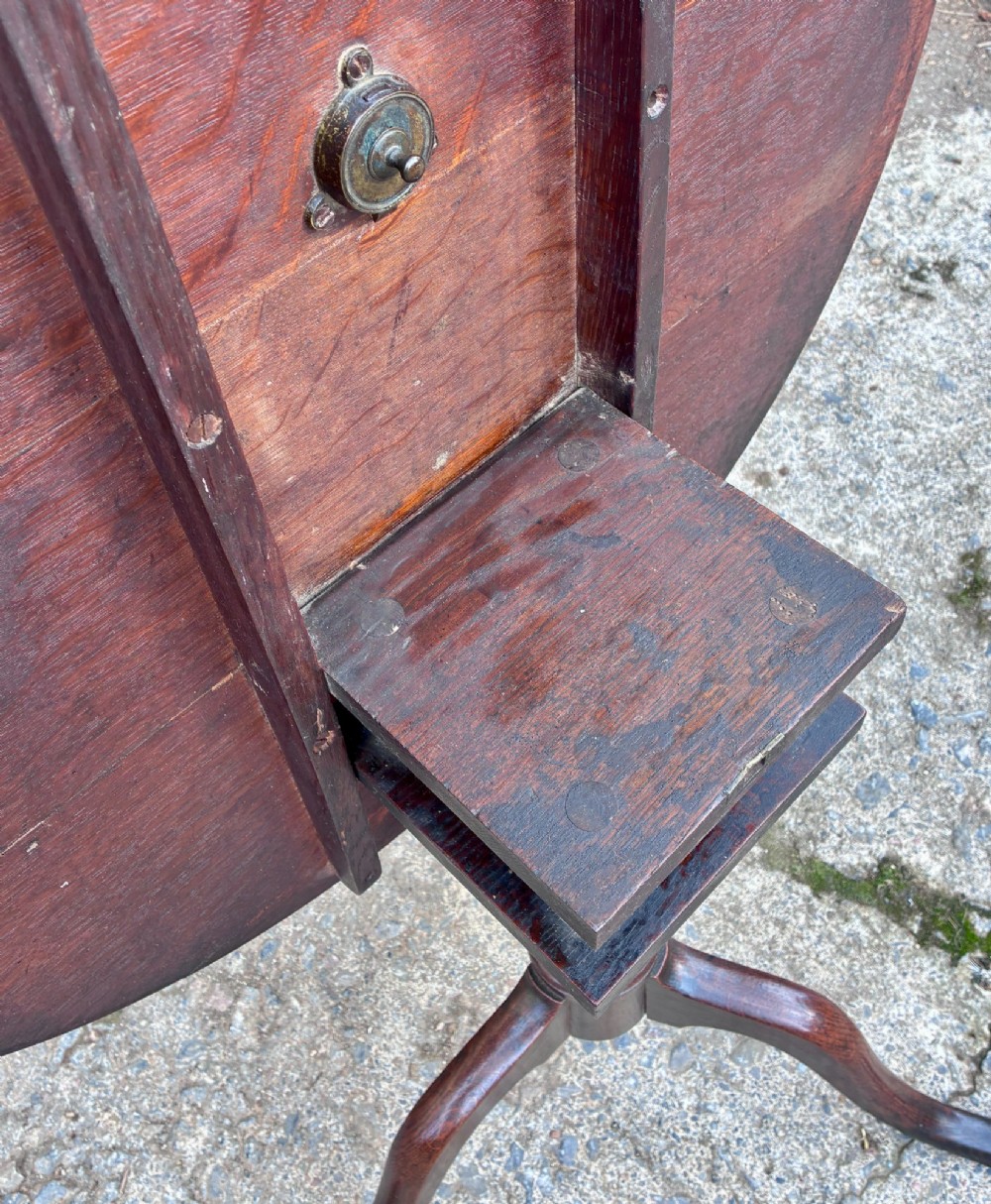 A dark brown Georgian oak tilt-top tripod table featuring a circular top, turned baluster column, and three cabriole legs. View XI