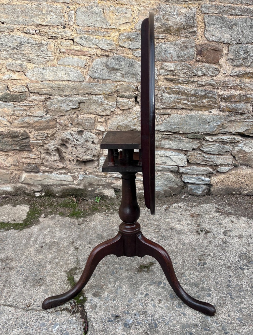 A dark brown Georgian oak tilt-top tripod table featuring a circular top, turned baluster column, and three cabriole legs. View XII