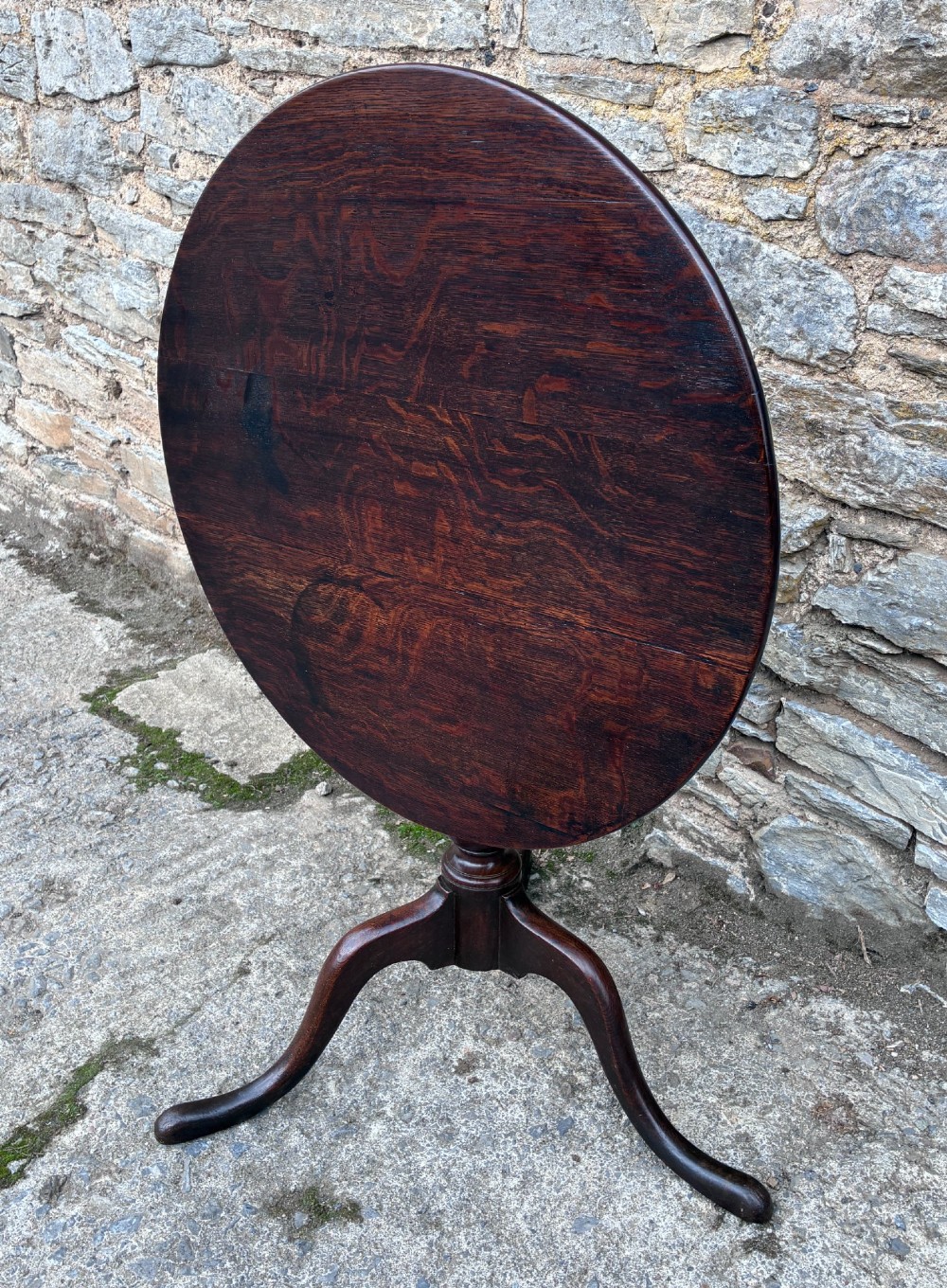 A dark brown Georgian oak tilt-top tripod table featuring a circular top, turned baluster column, and three cabriole legs. View XIV