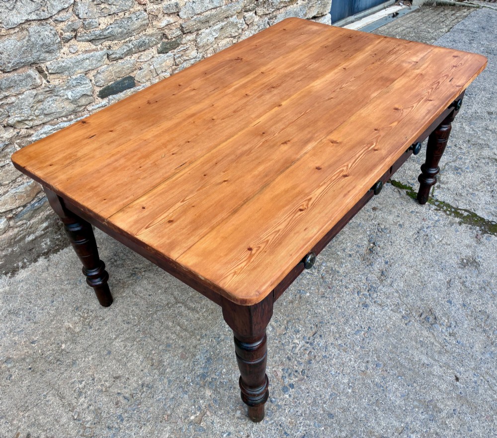 A Victorian pine farmhouse table featuring a light natural timber plank top, two frieze drawers with round wooden knobs, and four dark turned wooden legs. View IV