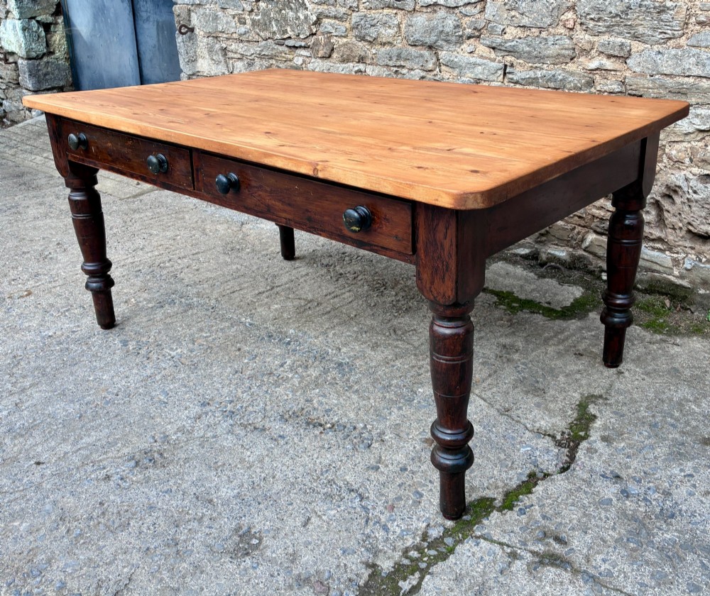 A Victorian pine farmhouse table featuring a light natural timber plank top, two frieze drawers with round wooden knobs, and four dark turned wooden legs. View VI