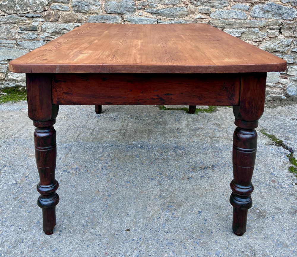 A Victorian pine farmhouse table featuring a light natural timber plank top, two frieze drawers with round wooden knobs, and four dark turned wooden legs. View XI