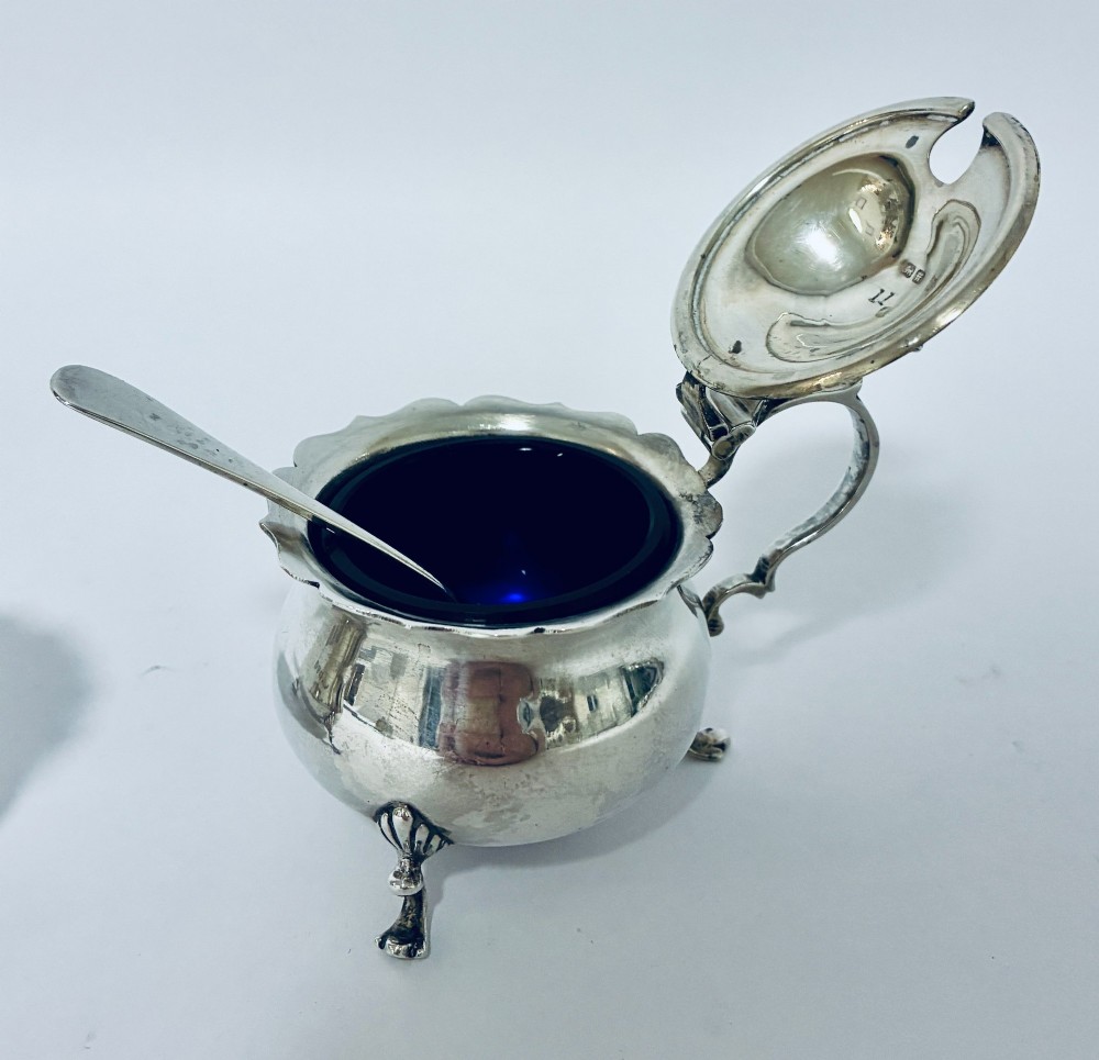 A three-piece silver cruet set comprising a pepper caster, open salt cellar, and mustard pot with a spoon, each resting on shell-adorned feet. View III