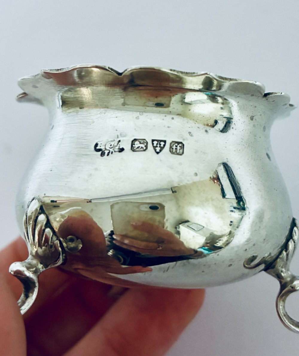 A three-piece silver cruet set comprising a pepper caster, open salt cellar, and mustard pot with a spoon, each resting on shell-adorned feet. View VIII