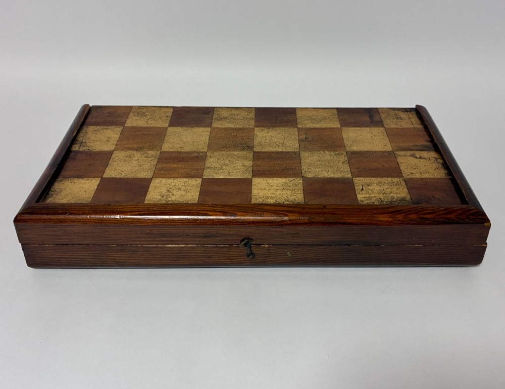An antique hinged wooden folding games board with a checkerboard surface, accompanied by turned draughts counters and a sliding wooden box containing chess pieces. View II