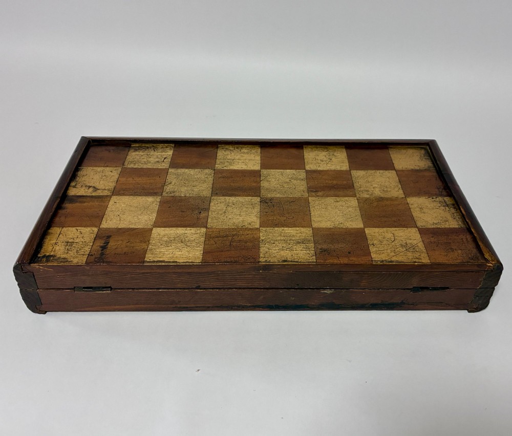 An antique hinged wooden folding games board with a checkerboard surface, accompanied by turned draughts counters and a sliding wooden box containing chess pieces. View III