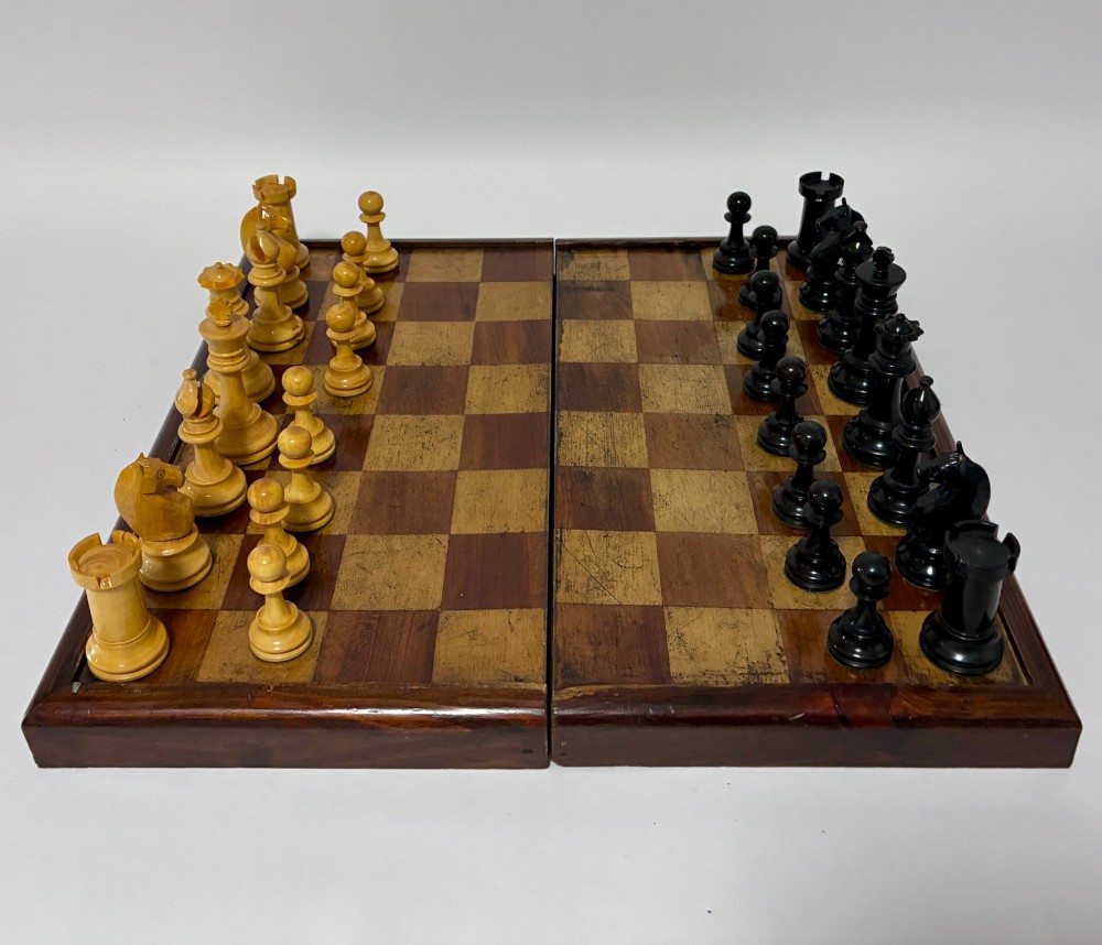An antique hinged wooden folding games board with a checkerboard surface, accompanied by turned draughts counters and a sliding wooden box containing chess pieces. View IX