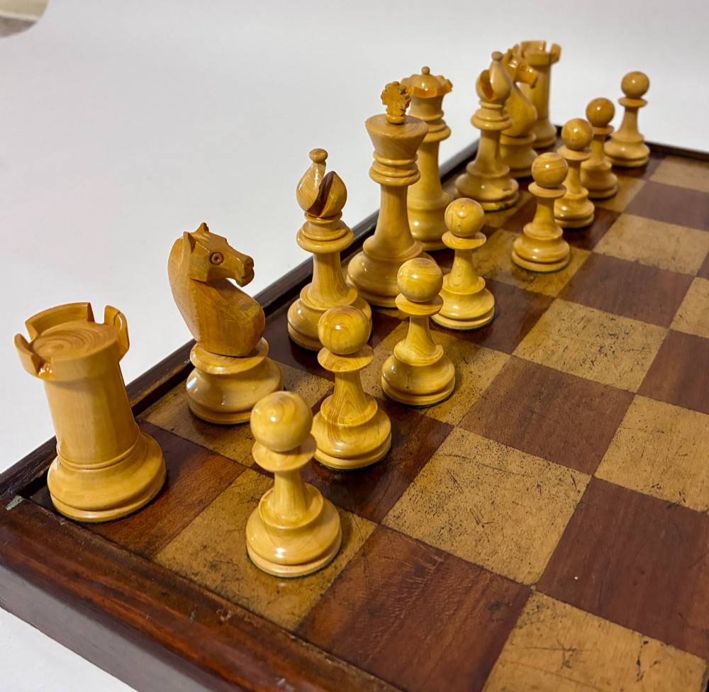 An antique hinged wooden folding games board with a checkerboard surface, accompanied by turned draughts counters and a sliding wooden box containing chess pieces. View X