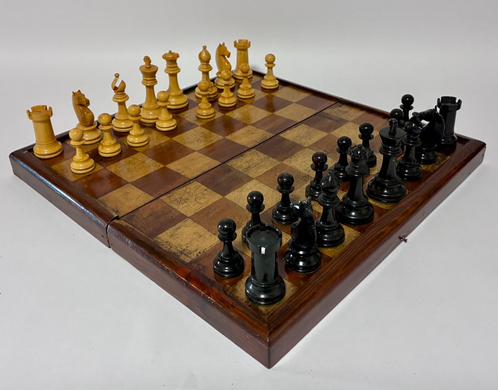 An antique hinged wooden folding games board with a checkerboard surface, accompanied by turned draughts counters and a sliding wooden box containing chess pieces. View XI