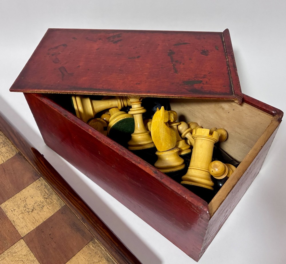 An antique hinged wooden folding games board with a checkerboard surface, accompanied by turned draughts counters and a sliding wooden box containing chess pieces. View XV