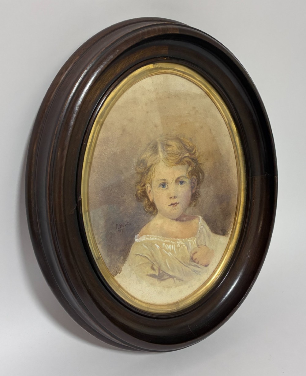 An oval Edwardian watercolour portrait depicting a young child with blonde curls, set inside a dark wooden frame with a gilt inner trim. View III
